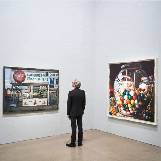 Das fotorealistische Digitalgemälde "Berlin" aus der Serie "Rueckenfiguren" von nostrokes zeigt einen Mann in einem schwarzen Anzug, der von hinten in einer Kunstgalerie steht. Er betrachtet zwei große, farbige Gemälde im Stil des Fotorealismus an einer weißen Wand. Das quadratische Werk ist in einer limitierten Edition auf Leinwand gedruckt und in der Online-Galerie ARTSPACER erhältlich.