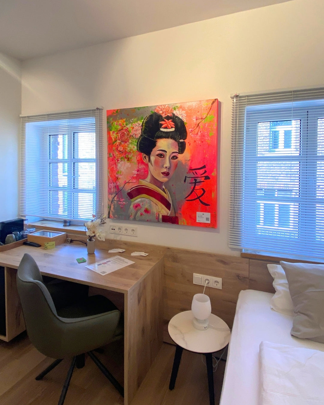 Porträt "Geisha" von Susann Versteegen (ARTSPACER). Eine Frau mit traditioneller Frisur vor einem leuchtenden, neon-pinken und grau-grünen, abstrakten Hintergrund, akzentuiert durch ein schwarzes Kanji-Schriftzeichen. Ausgestellt im Gutshaus am Rhein, Düsseldorf.