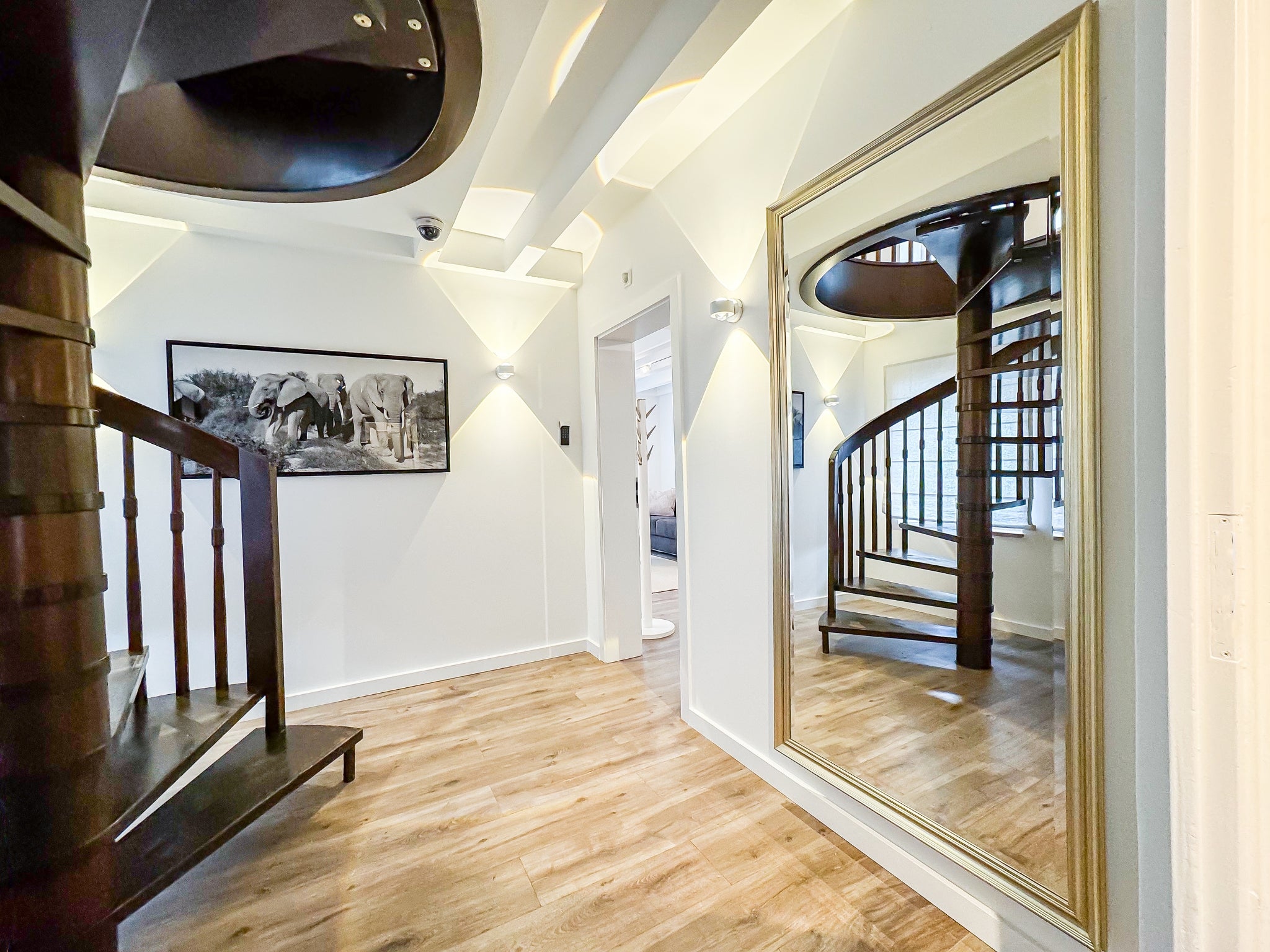 Ein heller, moderner Flur im Gutshaus am Rhein (Duisburger Landstraße 37, 40489 Düsseldorf) mit einer markanten Wendeltreppe aus dunklem Holz. Der Boden ist mit warmem Parkett in Holzoptik ausgelegt. Die stilvolle Unterkunft bietet erstklassigen Komfort für Reisende und kann zudem für exklusive Ausstellungen von Künstlern der Online-Galerie ARTSPACER gebucht werden.