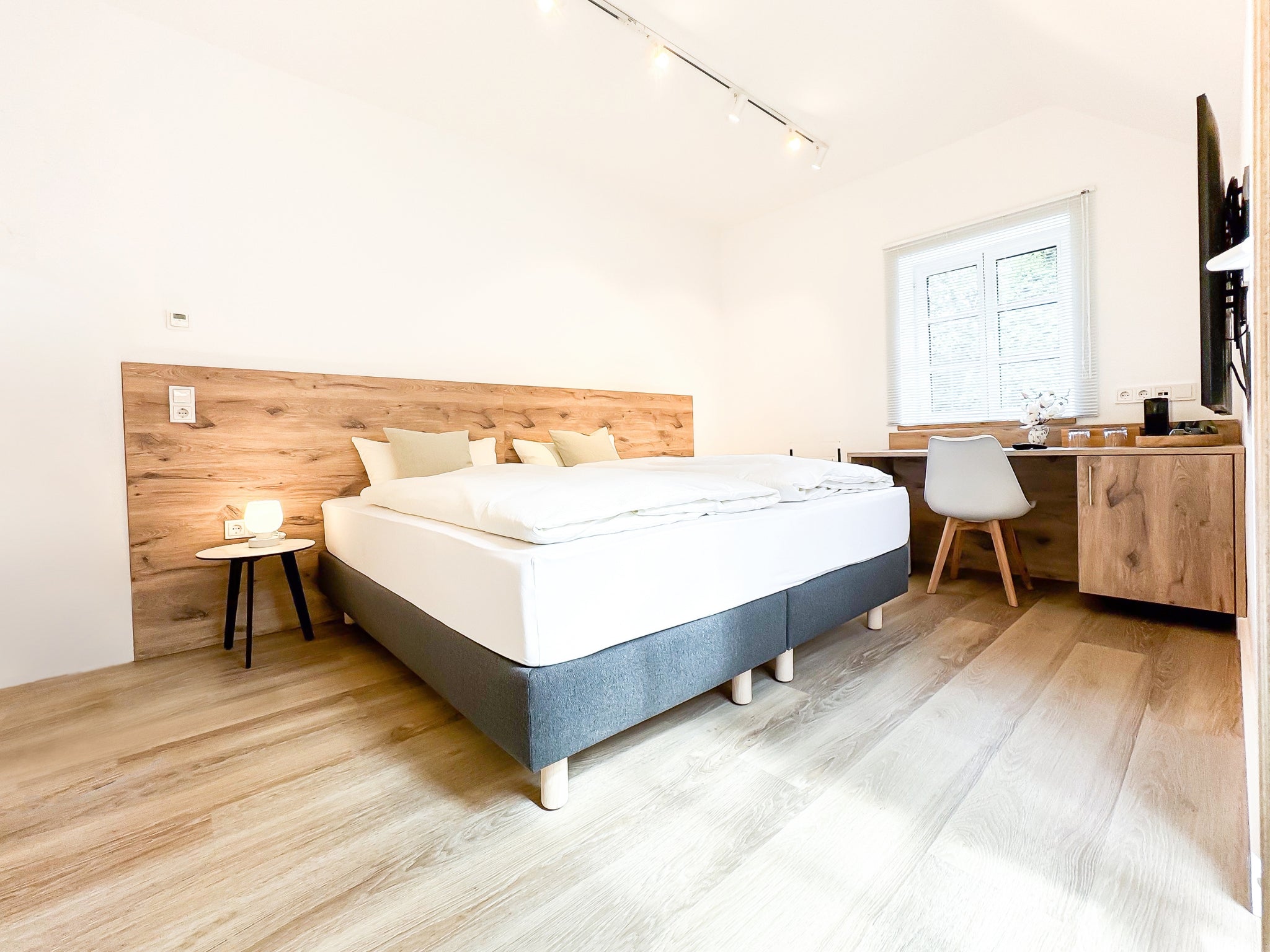 Ein helles, modernes Gästezimmer in den Art Apartments im Gutshaus am Rhein (Duisburger Landstraße 37, 40489 Düsseldorf). Das Zimmer bietet ein komfortables Boxspringbett mit Echtholz-Kopfteil, einen integrierten Schreibtisch am Fenster und hochwertigen Parkettboden. Die minimalistische Einrichtung schafft eine ideale Atmosphäre für Reisende und Kulturliebhaber. Wechselnde Ausstellungen von Künstlern der Galerie ARTSPACER.