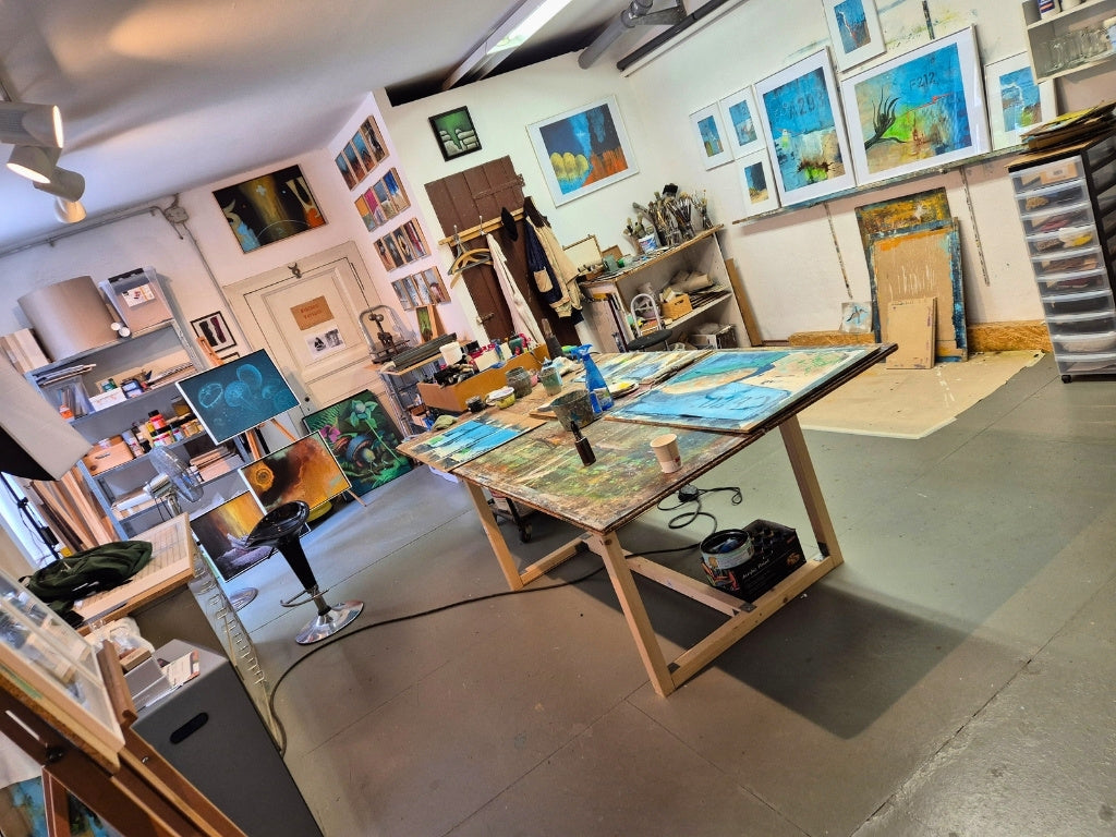 Blick in das Atelier von Peter Jaschinski in Wuppertal: Großer Arbeitstisch mit aktuellen abstrakten Werken, Farbtöpfen und Pinseln in einer hellen, kreativen Werkstatt.