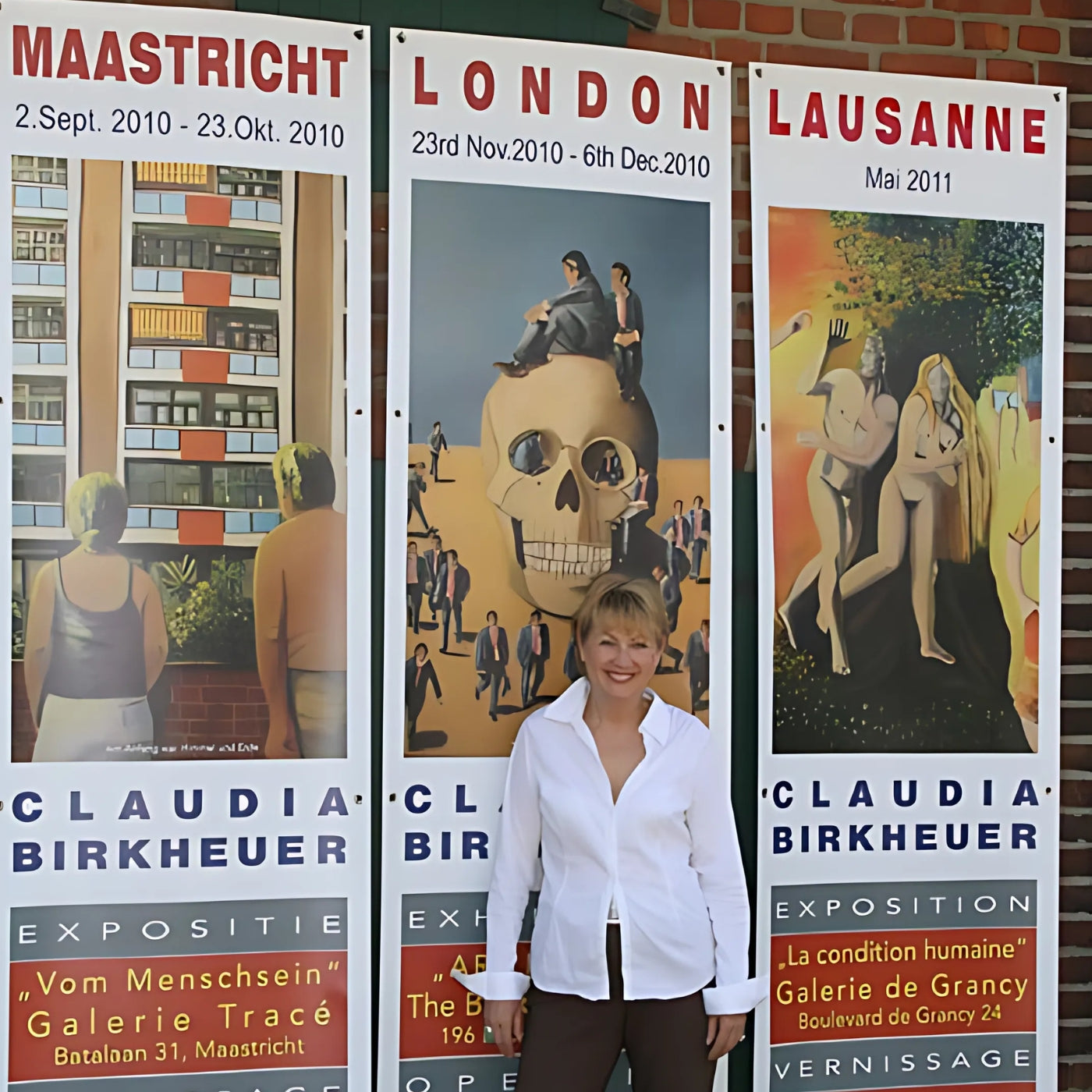 Claudia Birkheuer (ARTSPACER): Die Künstlerin steht lächelnd vor drei Plakaten ihrer Ausstellungen in Maastricht (2010), London (2010) und Lausanne (2011). Die Plakate zeigen Ausschnitte ihrer Kunstwerke und tragen ihren Namen sowie die Ausstellungsdaten und Orte.