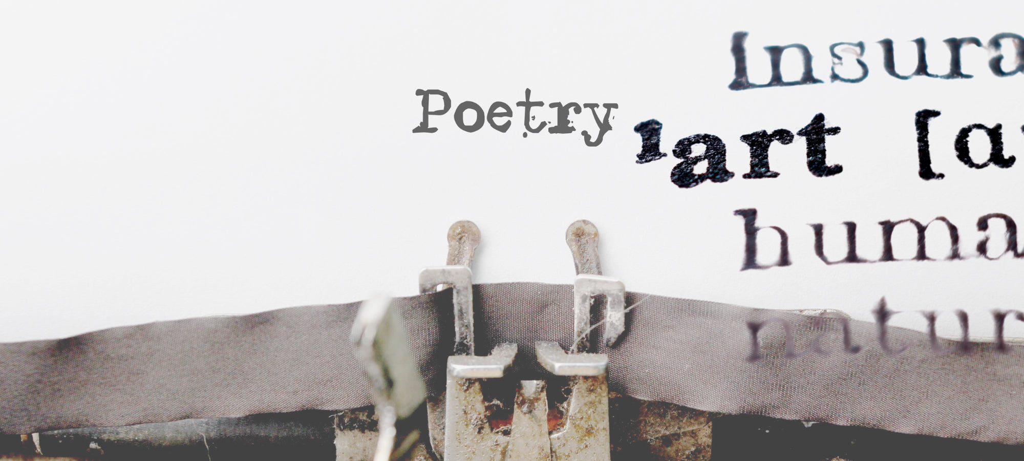 Nahaufnahme einer Schreibmaschine mit den getippten Wörtern ‚Poetry‘ und ‚art‘ auf weißem Papier; Headerbild für die Kategorie Wortkunst in der ARTSPACER Online-Galerie.