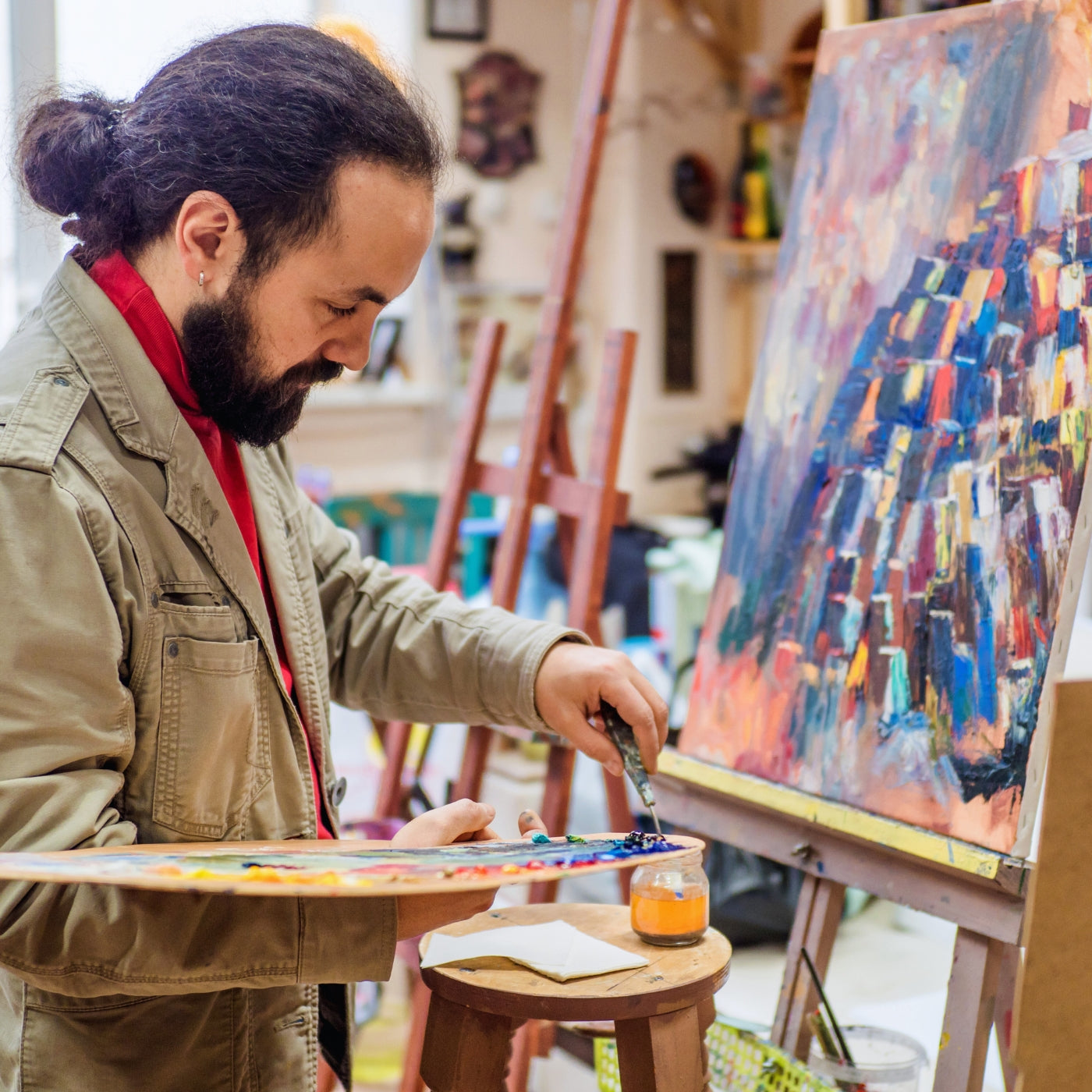 Künstler bei ARTSPACER arbeitet an einer farbenfrohen abstrakten Leinwand, umgeben von Kunstmaterialien und Staffeleien, die den kreativen Geist der Online-Kunstgemeinschaft verkörpern.