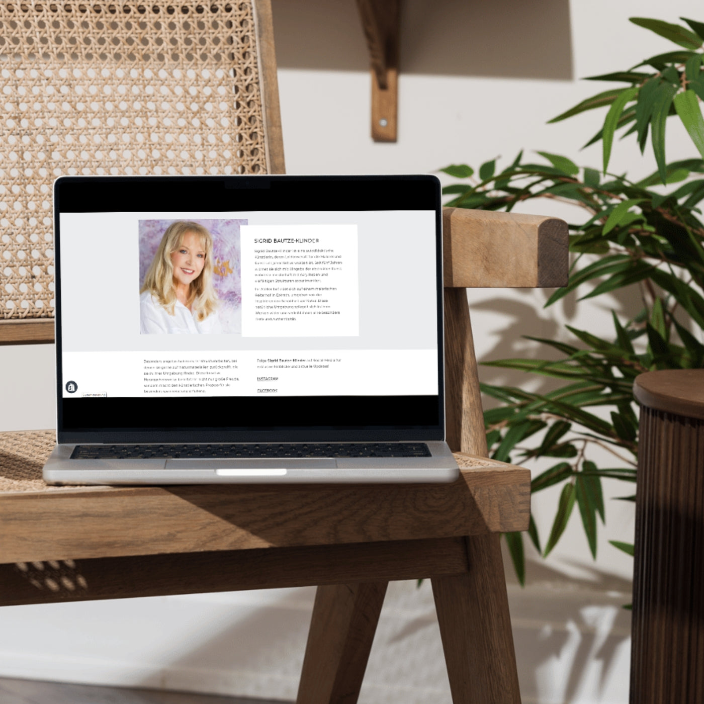 Laptop auf einem Holzstuhl zeigt die ARTSPACER-Online-Galerie mit einer Künstlerin vor abstrakter Pastellkunst in Rosa- und Weißtönen, beleuchtet von natürlichem Licht.