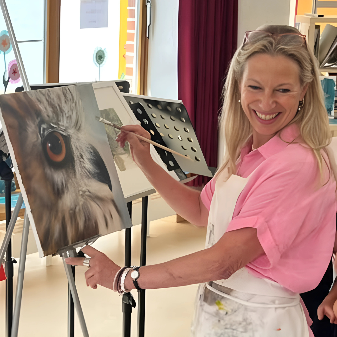 Anke Dinkelbach, Künstlerin von ARTSPACER, vor einer grünen Leinwand mit Pinsel in der Hand. Ihr konzentrierter Ausdruck und die Farbtupfer auf der Leinwand verraten ihre künstlerische Leidenschaft. Im Hintergrund sind weitere Gemälde mit Pferdeköpfen zu erkennen, die einen Einblick in ihr künstlerisches Schaffen geben.