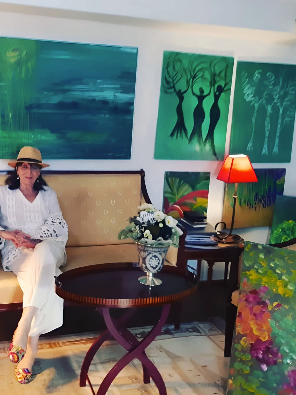 Federica (FEMARTSPACE) in ihrem Düsseldorfer Atelier: Die Künstlerin sitzt auf einem Sofa vor ihren großformatigen, grünen Gemälden. Ein Tisch mit Blumen steht davor, eine Lampe rechts. Ein weiteres Bild ist im Vordergrund sichtbar.