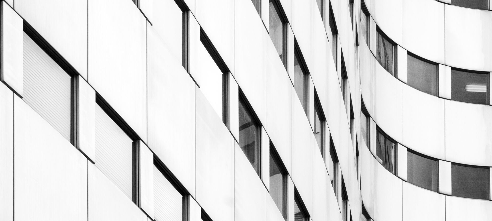 Abstrakte Schwarz-Weiß-Fotografie einer modernen Fassade mit rhythmisch angeordneten Fenstern, klaren geometrischen Linien und kontrastreichen Licht-Schatten-Effekten.