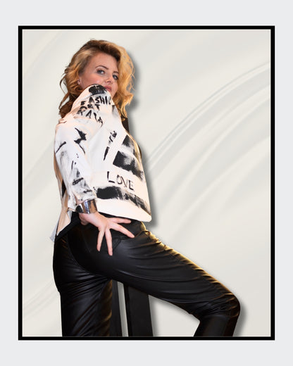 Eine blonde Frau steht vor einem cremefarbenen Hintergrund und blickt nach rechts. Sie trägt einen weißen Blazer mit schwarzen, abstrakten Mustern und Schriftzügen, darunter das Wort "LOVE". Darunter trägt sie ein schwarzes Oberteil und eine schwarze Hose. Fashionart von Kaja Schäfer, exklusiv bei ARTSPACER, Online-Galerie.
