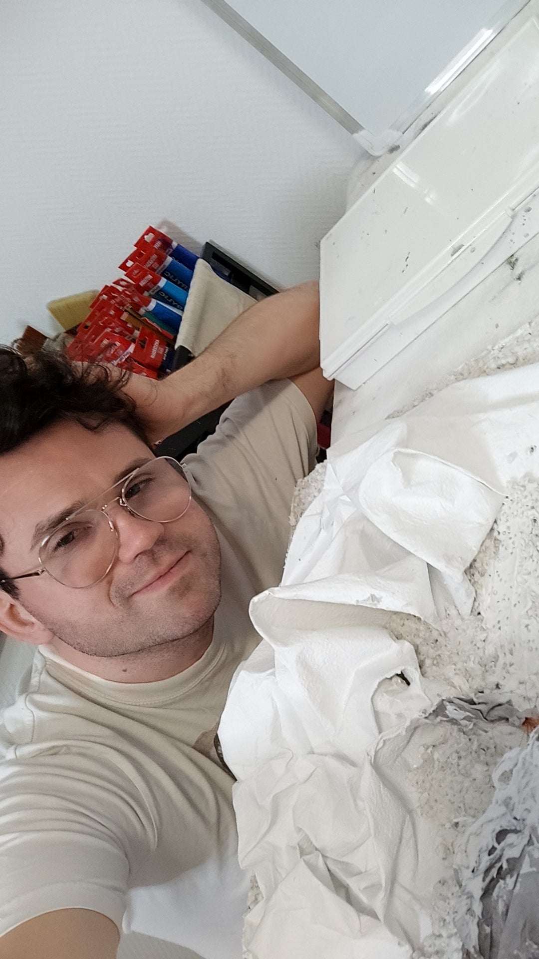 Eine Selfie-Perspektive des Künstlers, der neben einer großformatigen, weiß strukturierten Skulptur oder Leinwand am Boden liegt.