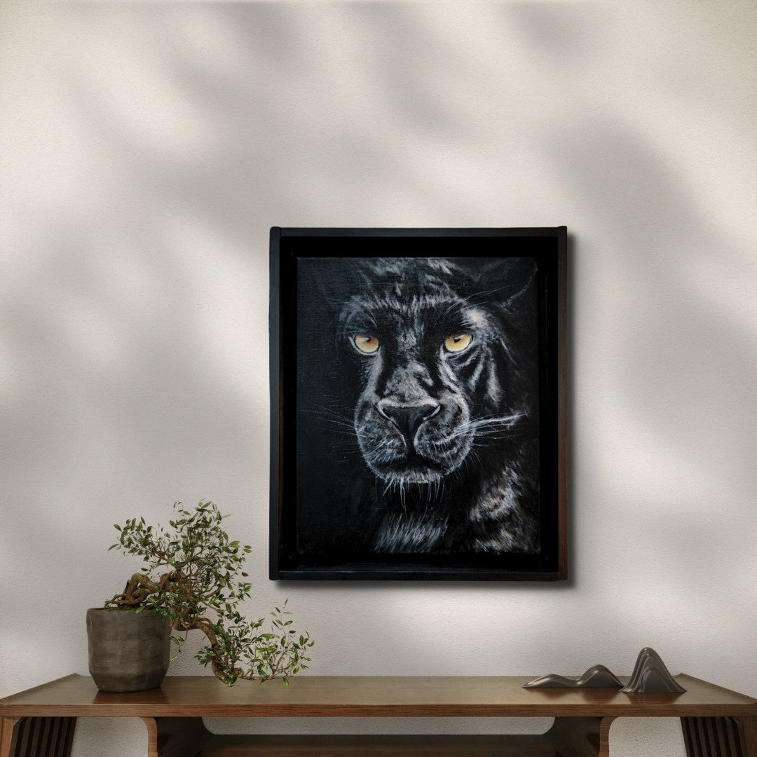 Acrylgemälde einer schwarzen Pantherin in Frontalansicht mit leuchtend gelben Augen vor tiefdunklem Hintergrund, gerahmt in einem schwarzen Schattenfugenrahmen.