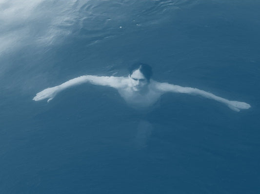 Das Kunstwerk "Christianisierung Brandenburgs" des Künstlers nostrokesbitte zeigt ein digitales Gemälde im fotorealistischen Stil. Es ist ein Porträt, das eine Person von oben im Wasser liegend darstellt. Die Person blickt direkt auf den Betrachter und hat die Arme ausgebreitet. Das Bild ist in kühlen, bläulichen Farbtönen gehalten, die die Wasseroberfläche darstellen. Das Werk wurde auf Leinwand gedruckt und ist in einer limitierten Edition über die Online-Galerie ARTSPACER erhältlich.