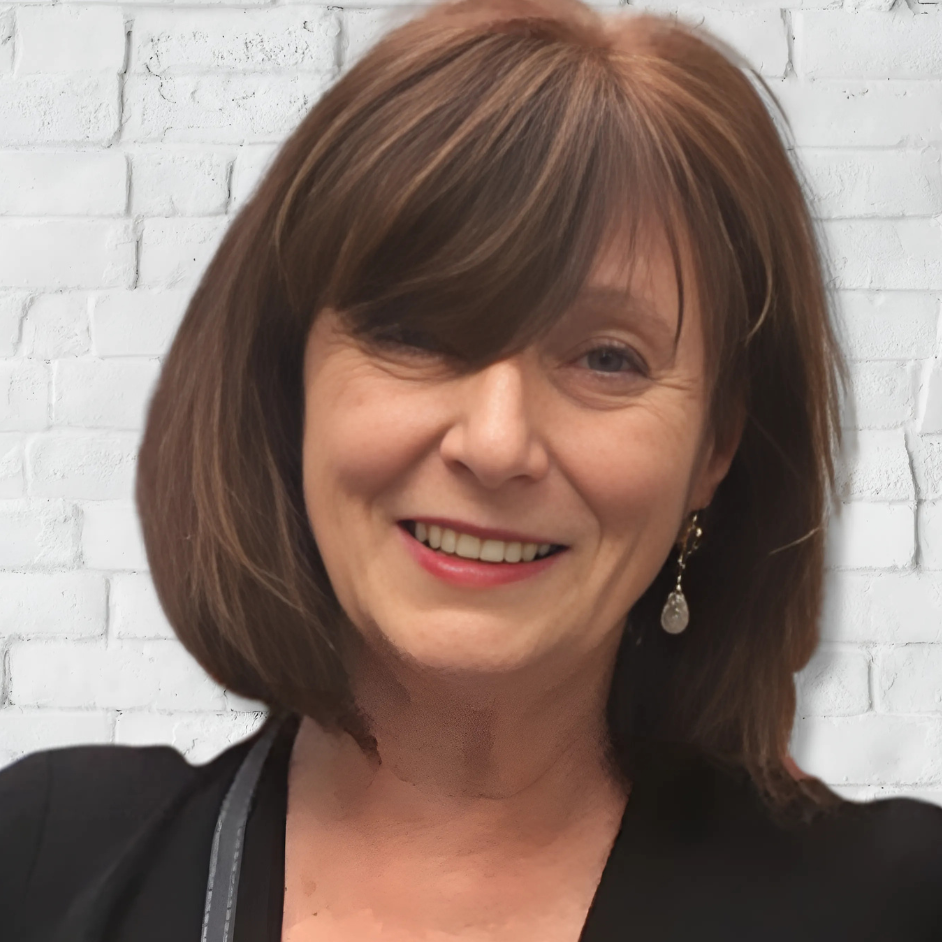 Person mit schulterlangem braunem Haar vor einer weißen Backsteinwand; dunkle Kleidung und dezente Lichtstimmung.