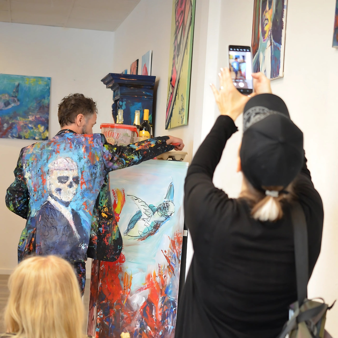 Künstlerin Simone Kratzsch (von hinten) mit schwarzer Mütze fotografiert mit ihrem Smartphone einen Mann in einem farbenfrohen Jackett mit Totenkopf-Motiv (Karsten Breidenbroich)