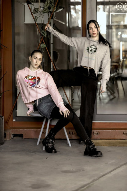 Ein kurz geschnittener, rosafarbener Hoodie mit überschnittenen Schultern. Extralange Bündchen mit Daumenloch und eine bedruckte Kunstgrafik auf der Vorderseite. Mode von Soulfashion.