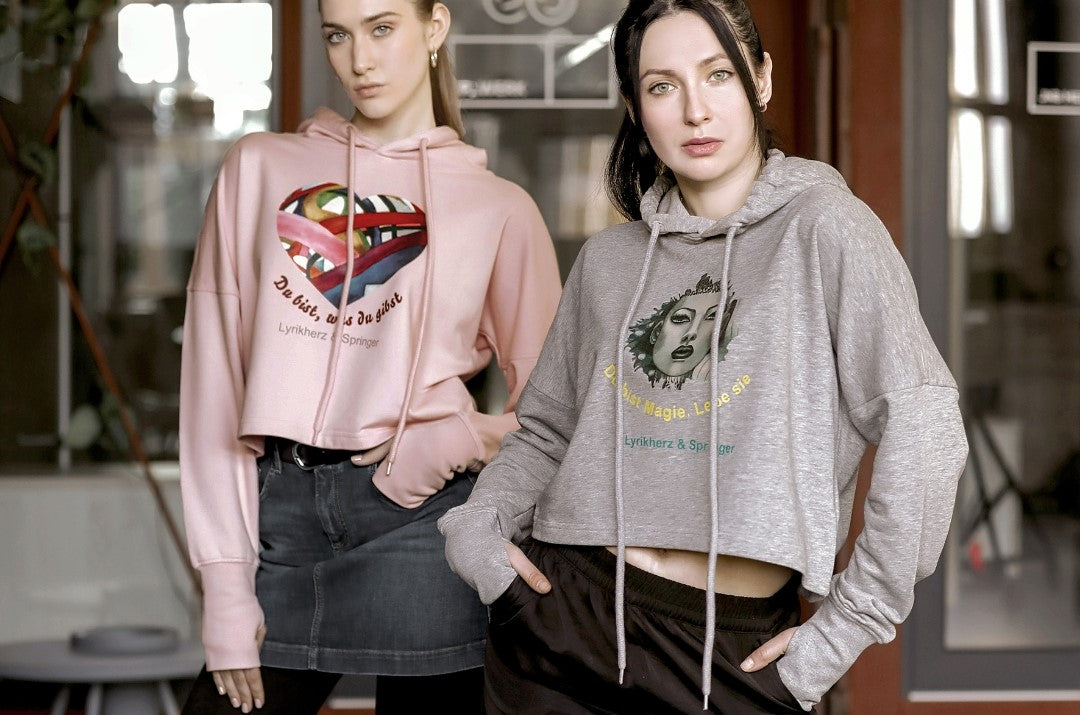 Ein kurz geschnittener, rosafarbener Hoodie mit überschnittenen Schultern. Extralange Bündchen mit Daumenloch und eine bedruckte Kunstgrafik auf der Vorderseite. Mode von Soulfashion.