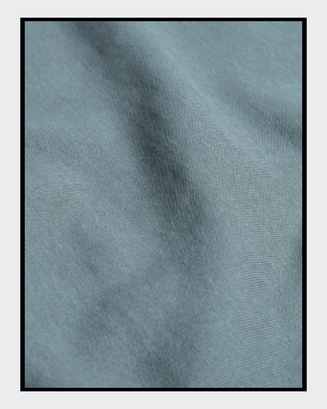 Stoffdetail von: Ein nebelblauer Unisex-Hoodie mit einer Kängurutasche und Kapuze. Auf der Vorderseite ist ein Kunstwerk aufgedruckt: Es zeigt eine stilisierte Frau mit Brille in Collagen-Optik, begleitet von Text in Gelb und Rot. 