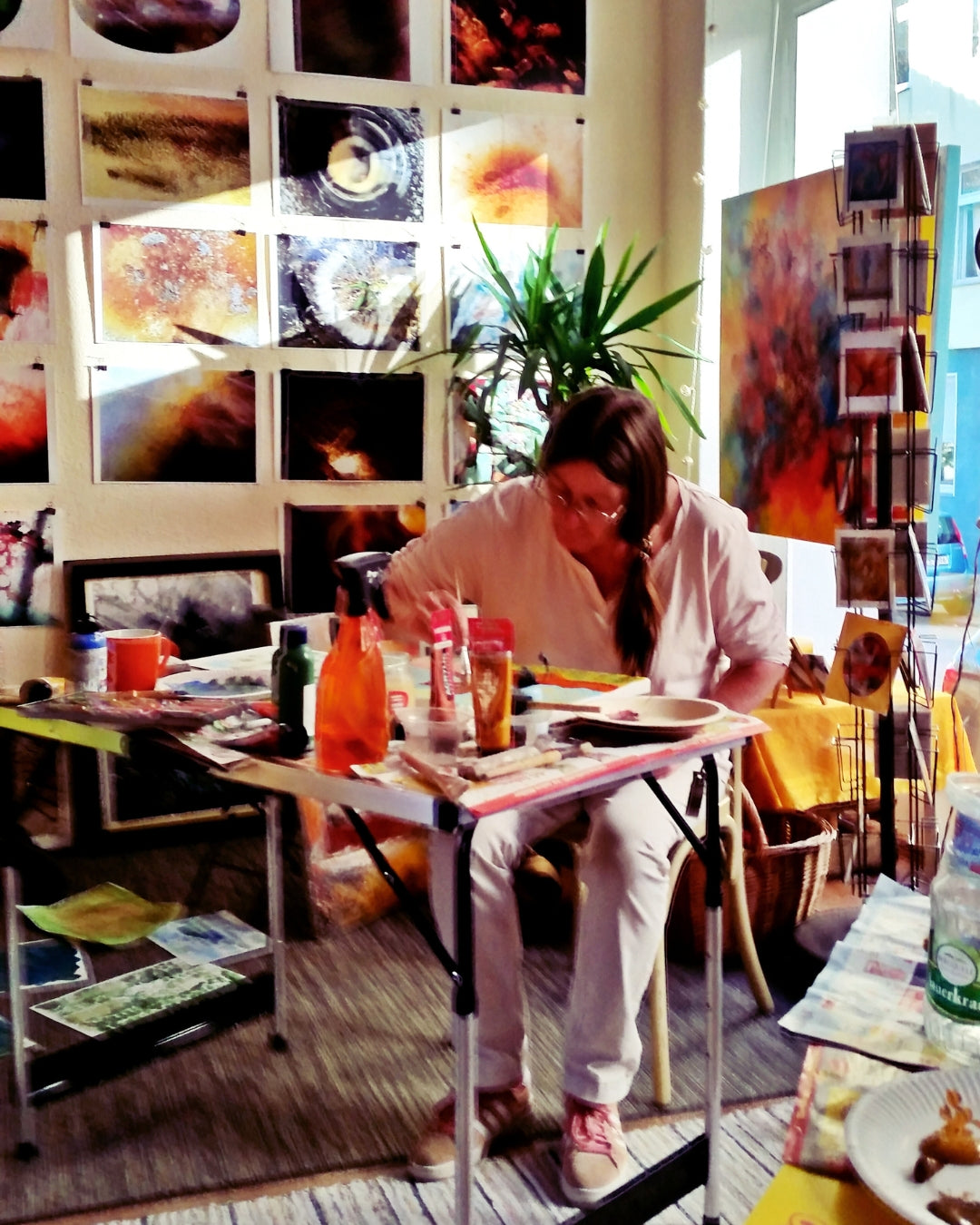 In einem hellen, kreativen Raum der Wuppertaler Galerie Paletti leitet die Künstlerin Susanne Stepbach einen Workshop. Teilnehmer arbeiten an verschiedenen Kunstprojekten, umgeben von bunten Materialien und inspirierenden Kunstwerken. Die Atmosphäre ist lebhaft und einladend.