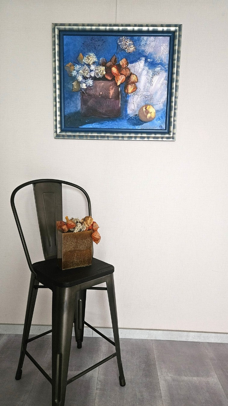 Expressives Stillleben von Vera Stein in Blau und Braun. Eine klobige, dunkle Vase hält weiße, getrocknete Blumen und leuchtend orangefarbene Physalis-Lampions. Der Hintergrund ist eine stark strukturierte Fläche in tiefem und hellem Blau, unterbrochen von einem breiten weißen Pinselstrich. Rechts unten liegt eine runde, gelbe Frucht.